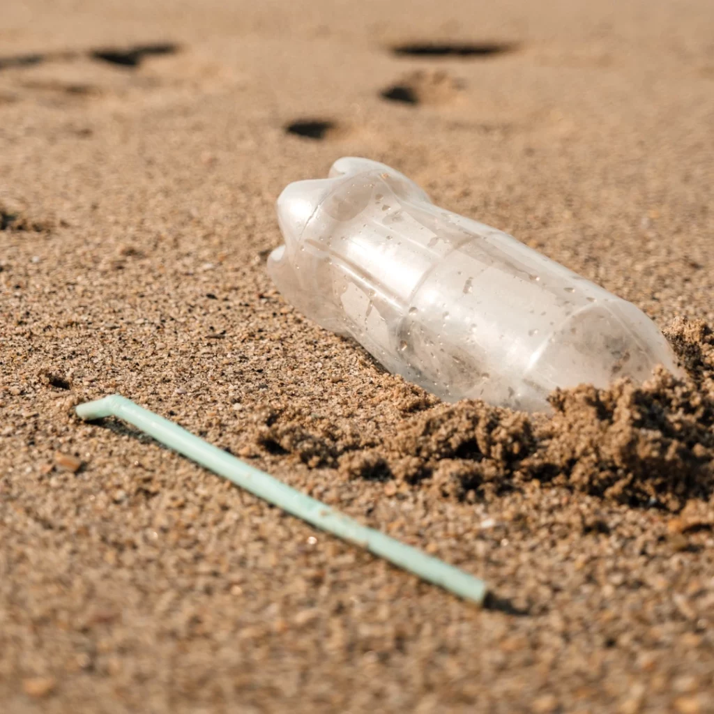 Déchets d'une bouteille et d'une paille en plastique dans le sable
